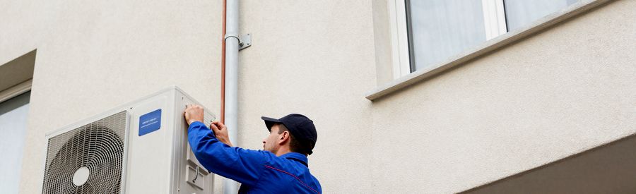 technicien pose unité extérieure pompe à chaleur immeuble résidentiel